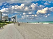 white sand beach near city buildings under blue and white sunny cloudy sky during daytime